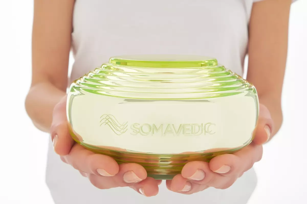 Vedic grün 3 Grüner Glasbehälter mit der Aufschrift Somavedic der von einer Frau in beiden Händen gehalten wirds